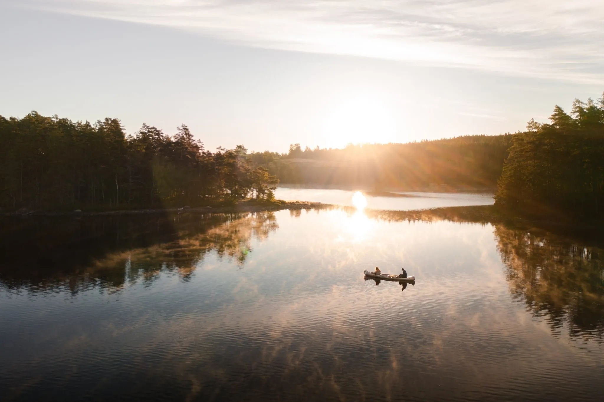 A canoe with two paddlers on a calm lake at sunrise, sun glare on the water