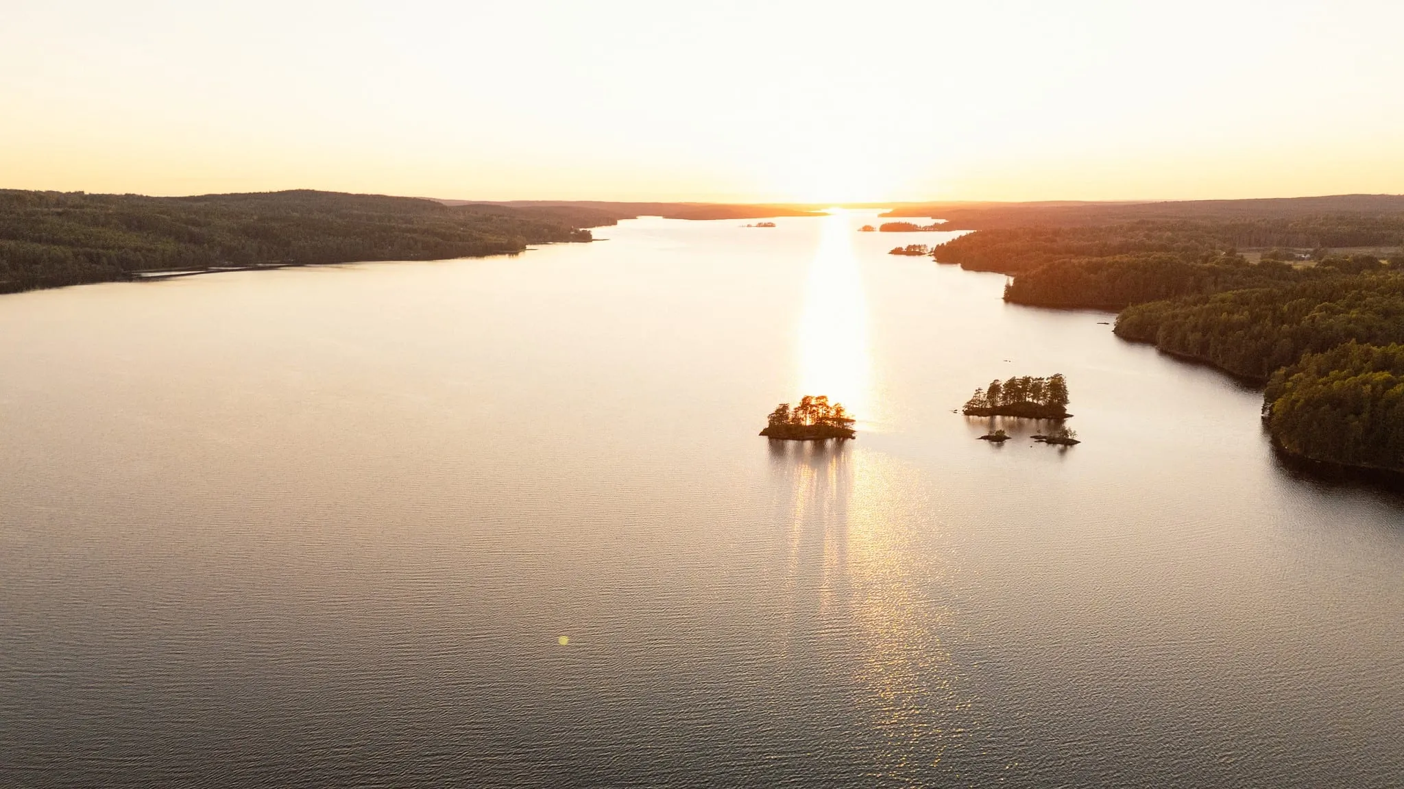 Two small wooded islands on a wide lake at sunset, seen from above