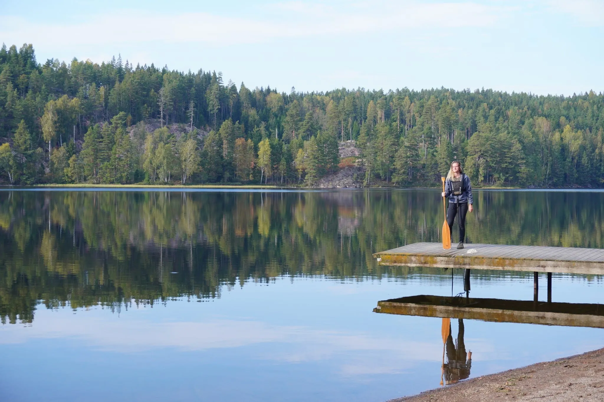 A paddler with a paddle on a wooden jetty by a calm forest lake