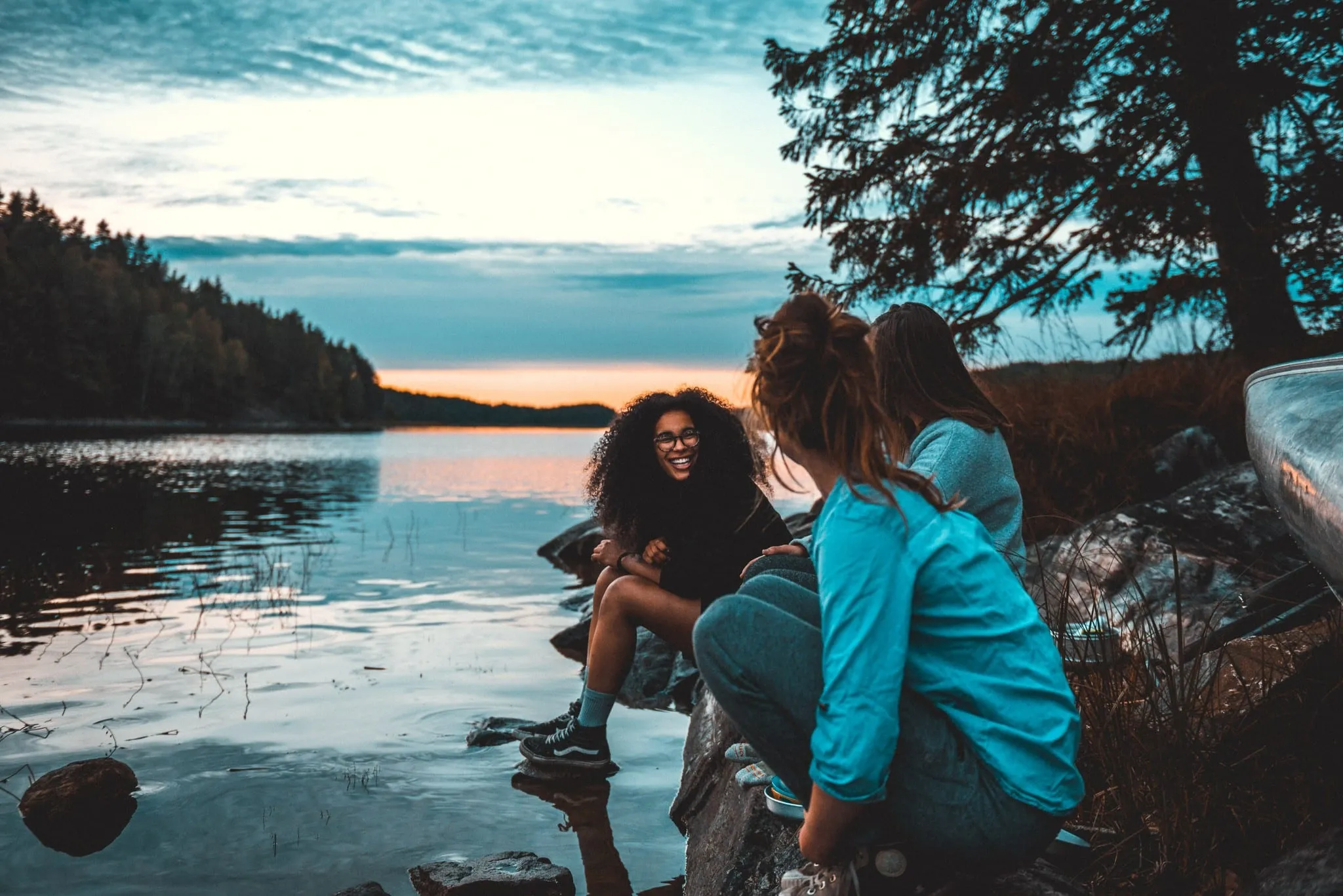 Three friends laughing by a lake at dusk
