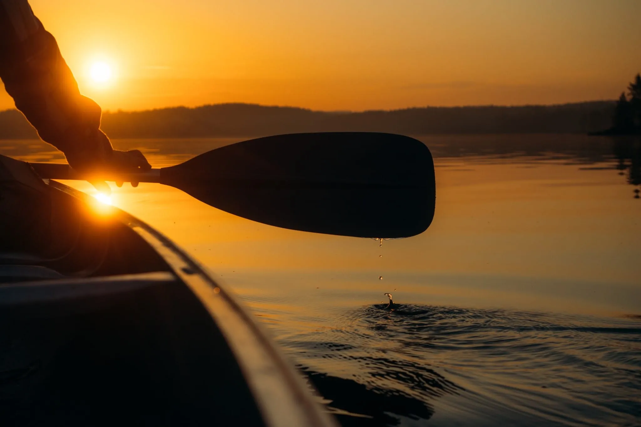 A paddle silhouetted against the sun setting over a lake